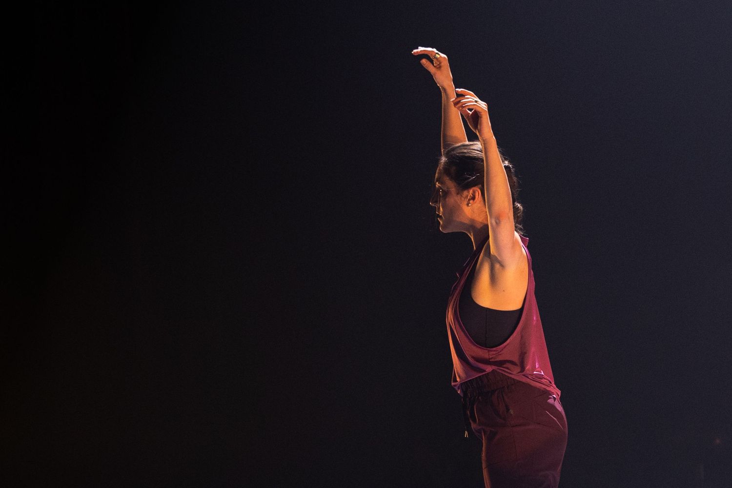 Modern dancer in plum-colored top performs expressive contemporary dance movements against black backdrop.