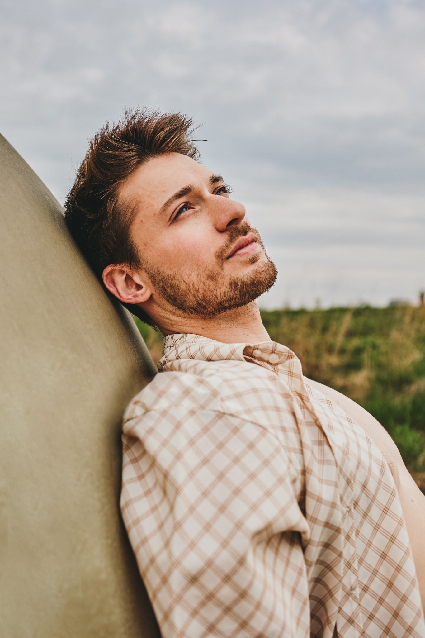 Person in a plaid shirt looking up against cloudy sky and wall in outdoor setting.