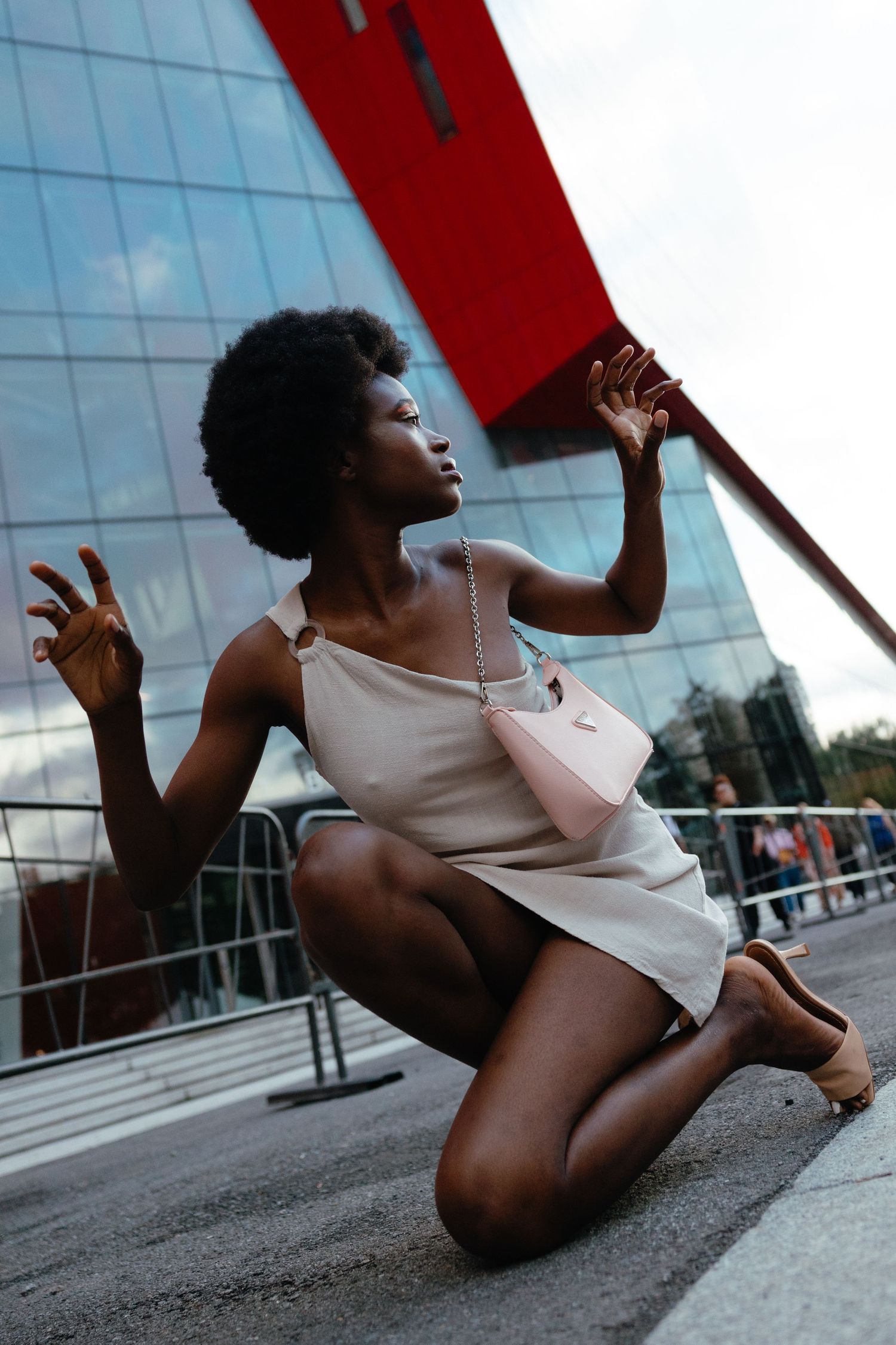 A dancer in a white dress strikes an artistic pose against an urban backdrop with glass buildings and red architectural elements.