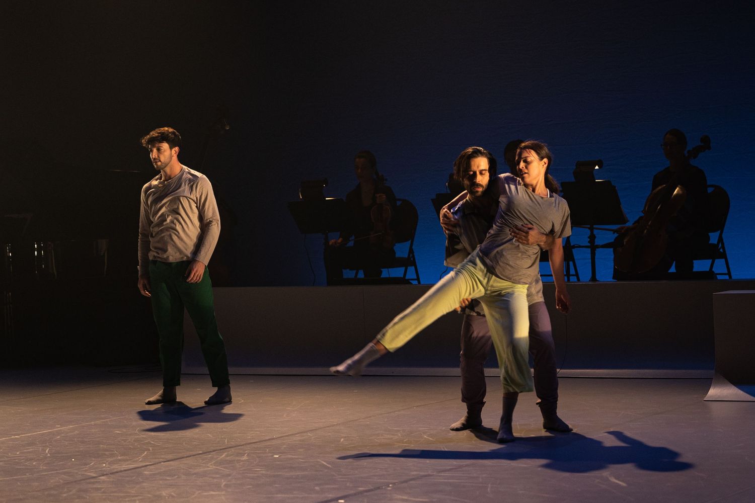 Dancers perform on a dimly lit stage with silhouetted figures in the background during a contemporary dance piece.