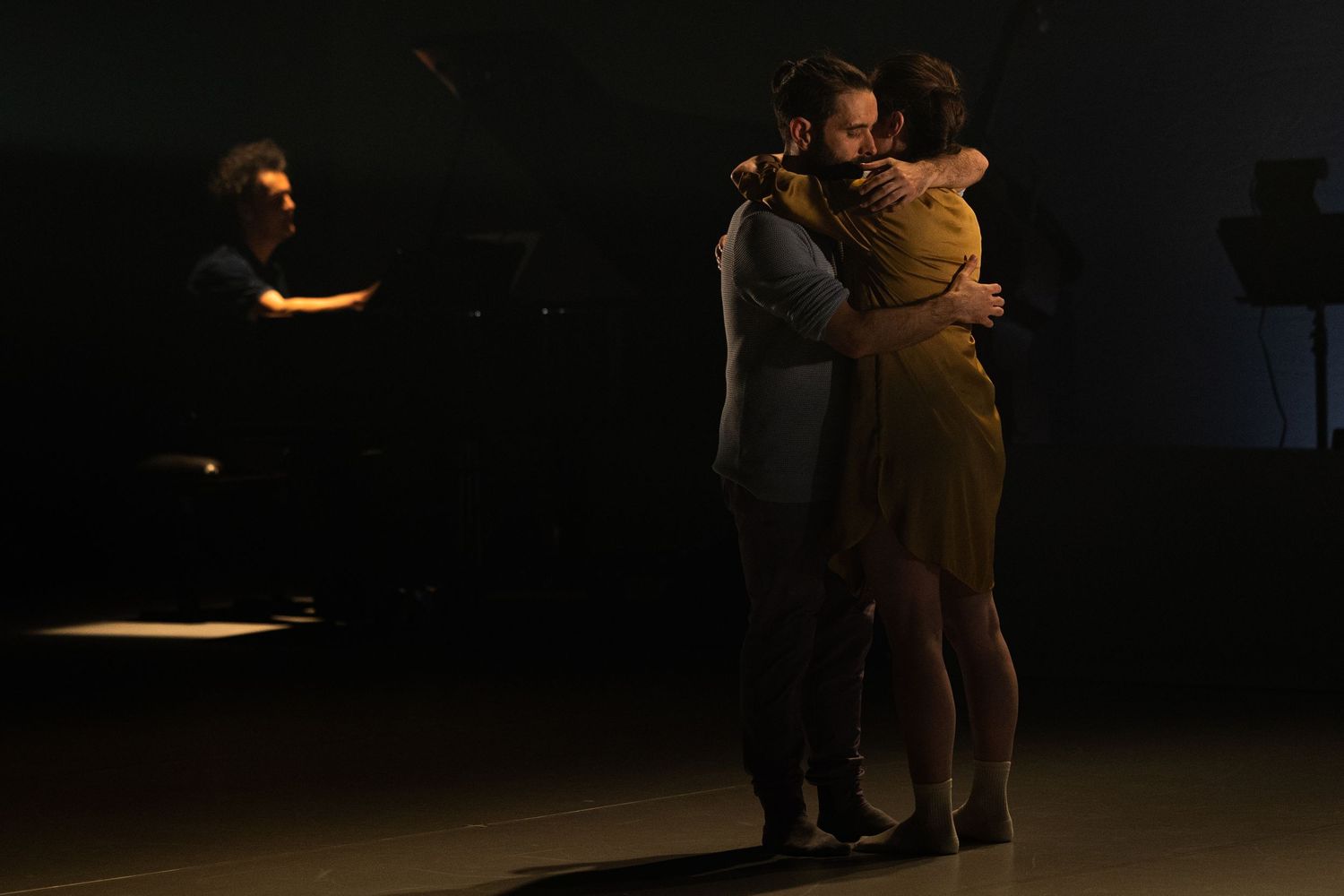 Dancers perform an emotional contemporary dance duet on a dimly lit stage.