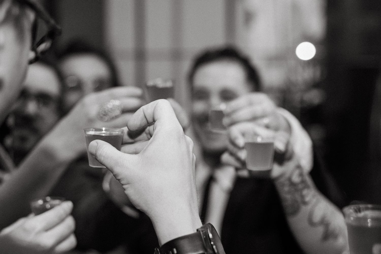 People raise small shot glasses during a festive toast in black and white photography.