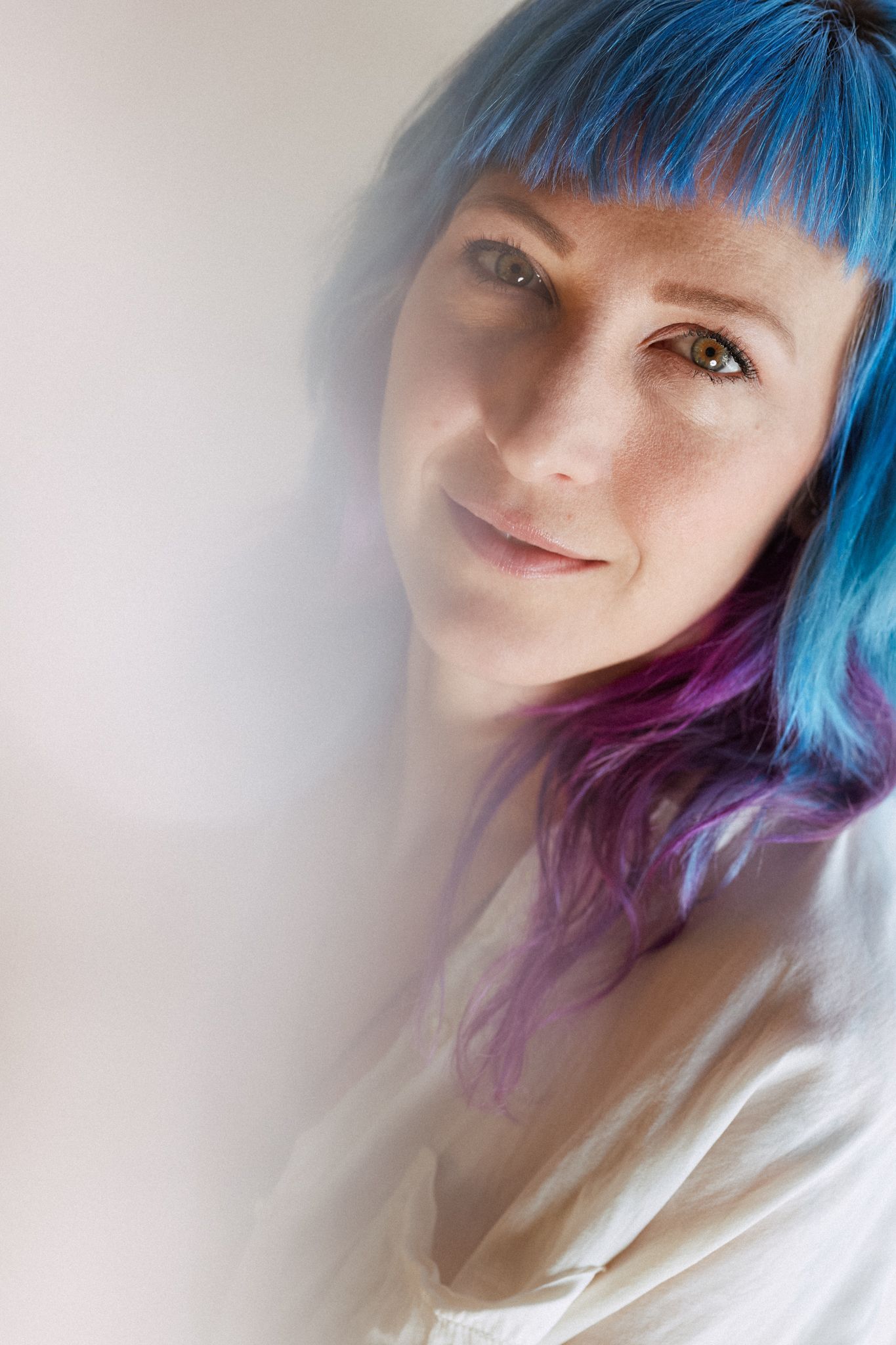 A person with bright blue and purple ombre hair smiles softly in a series of dreamy, ethereal selfie portraits.