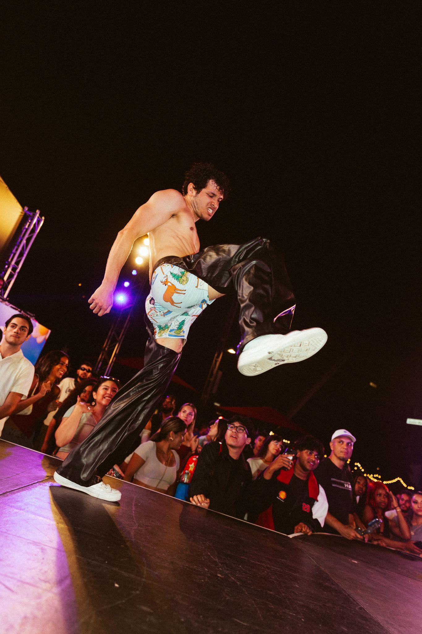 Dynamic breakdancers perform acrobatic moves on a dark stage with colorful spotlights illuminating their performance.