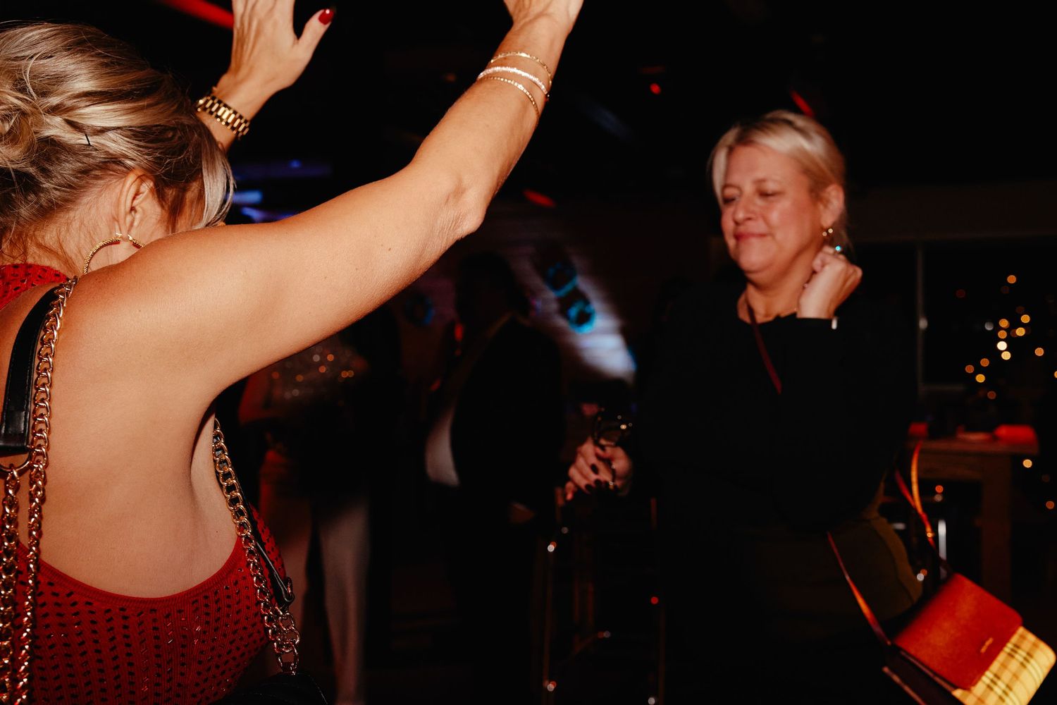 People dancing and celebrating at a lively nighttime party with red ambient lighting and festive atmosphere.