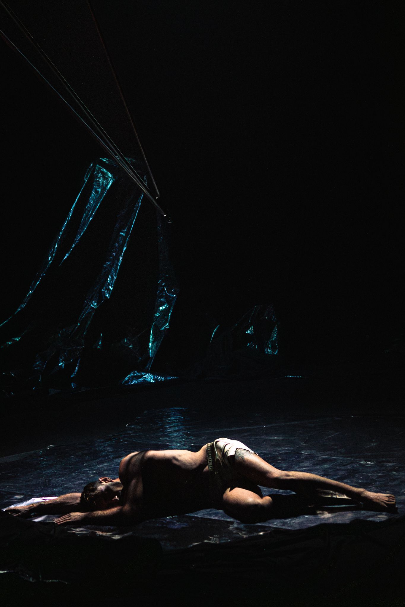 A dramatic sequence of still photos showing a dancer laying on a dark stage floor in various positions with theatrical lighting.