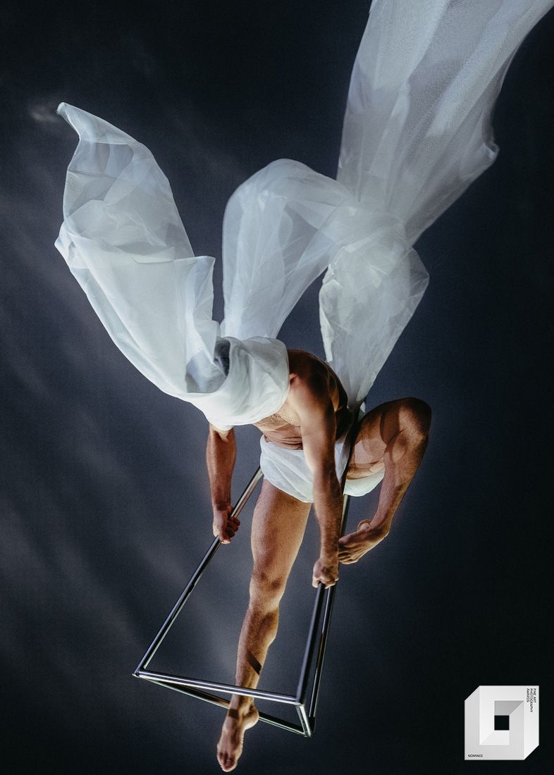 A flowing white fabric reveals a dancer's arms and legs in graceful movement against a black background in sequential shots.