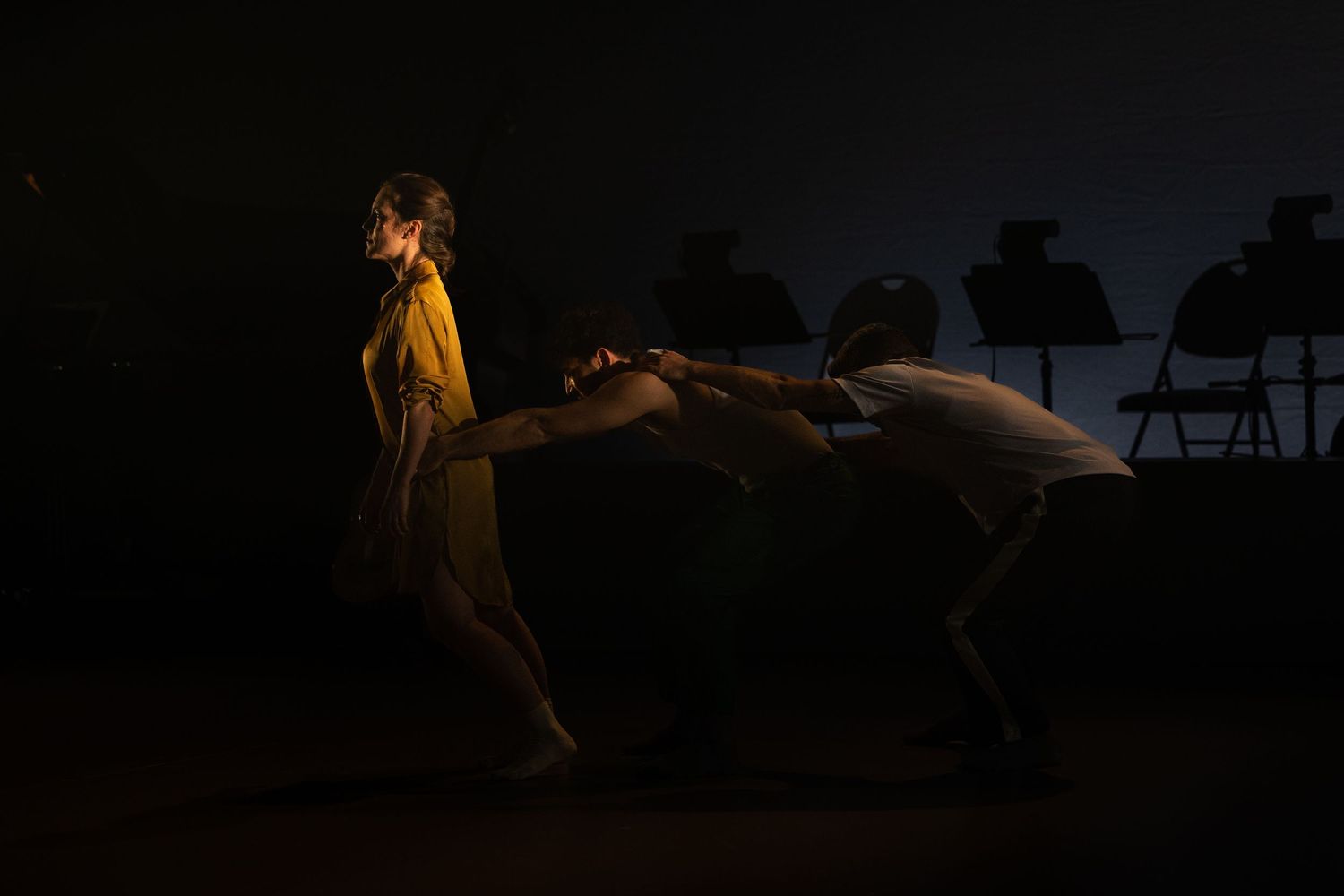 Silhouettes of performers on stage during a theatrical production with dramatic lighting effects.