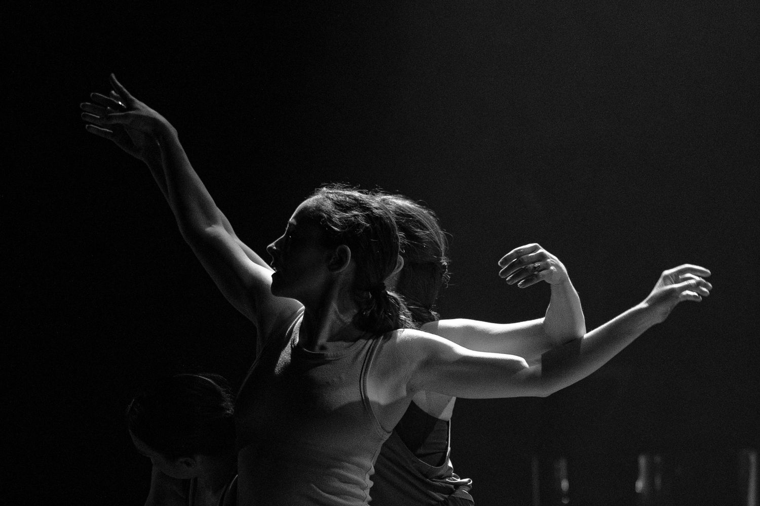 High contrast black and white silhouettes of dancers performing a contemporary dance sequence in a dark studio space.