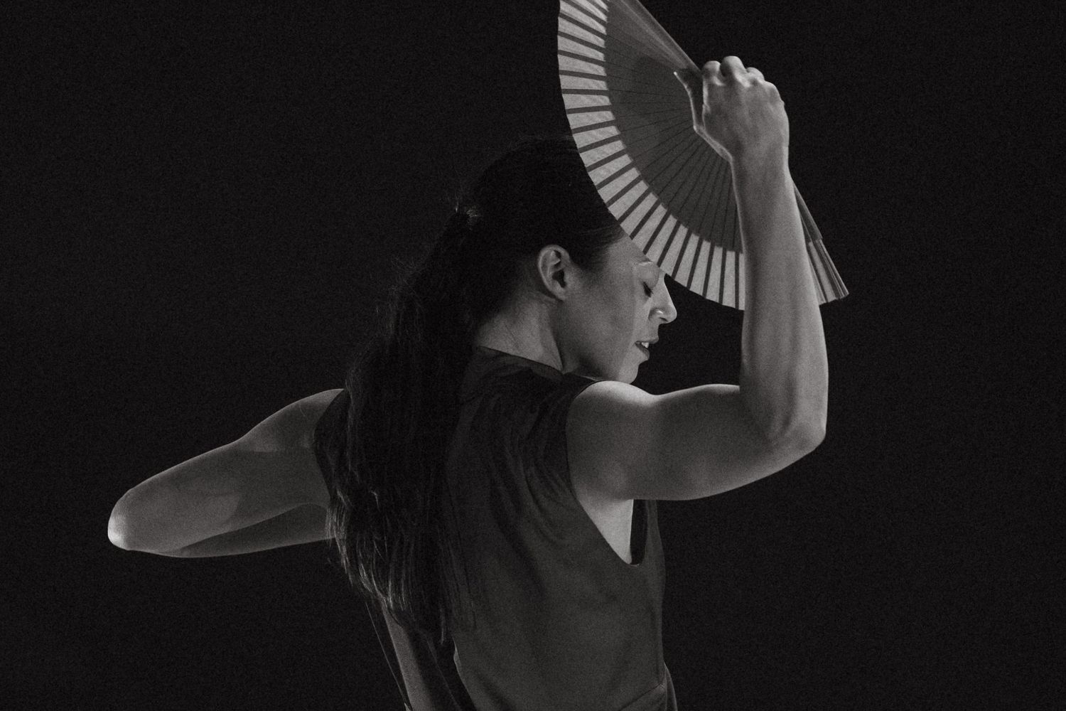 Dramatic black and white profile view of a dancer with a fan creating an elegant silhouette against dark background.