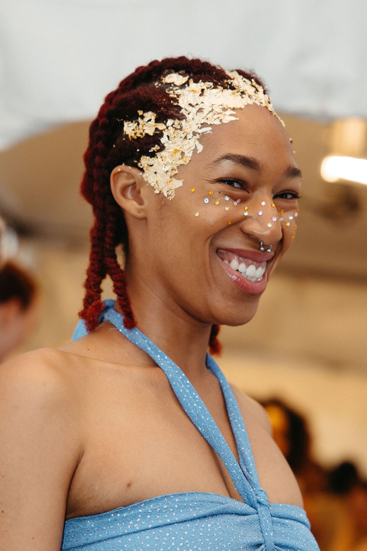 Portrait showing joyful smile wearing light blue halter top, with decorative glitter accents and braided hairstyle.