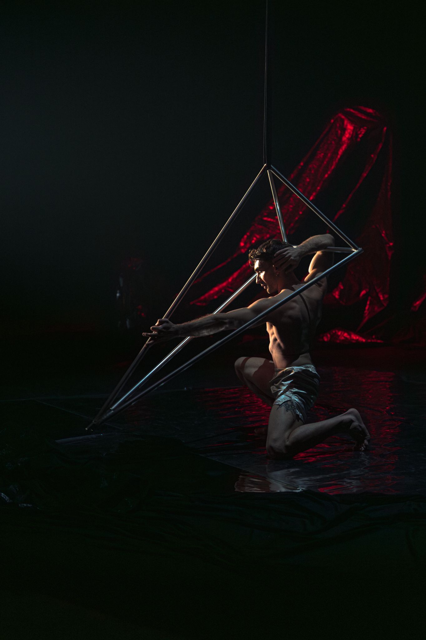 Dramatic performance art sequence featuring aerial acrobatics with glowing geometric structures in low light.