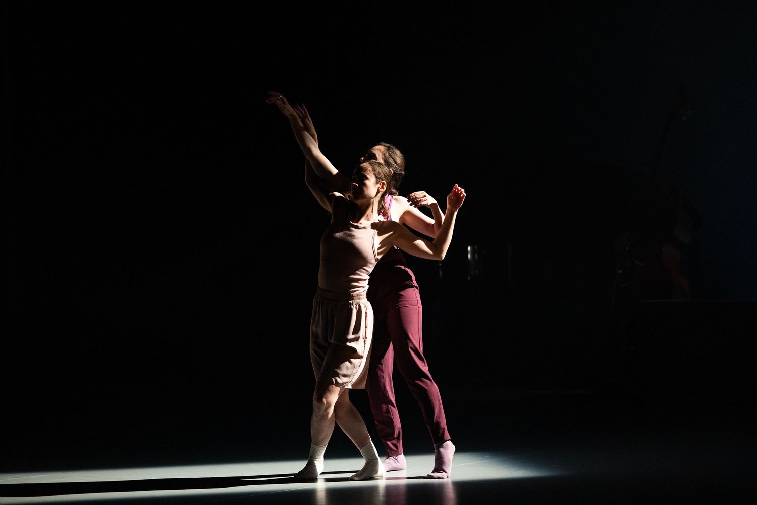 Two dancers perform a dynamic contemporary duet under dramatic spotlighting on a dark stage.