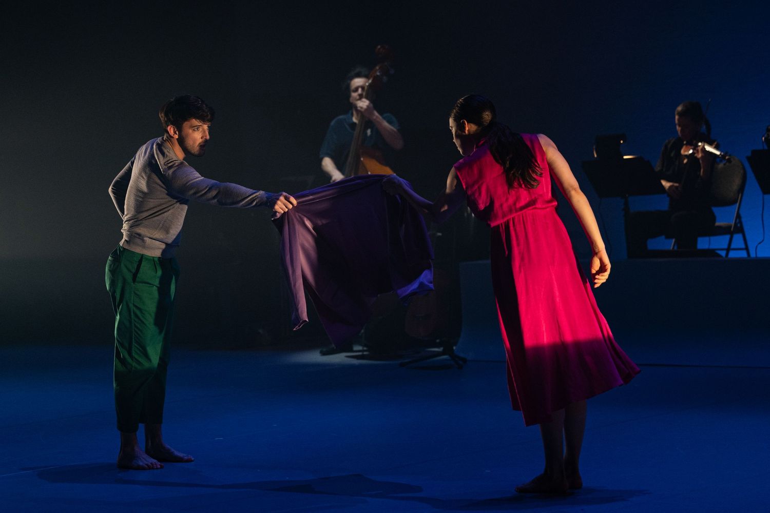 Stage performance featuring dancers in colorful costumes on a dark blue-lit stage during a theatrical production.