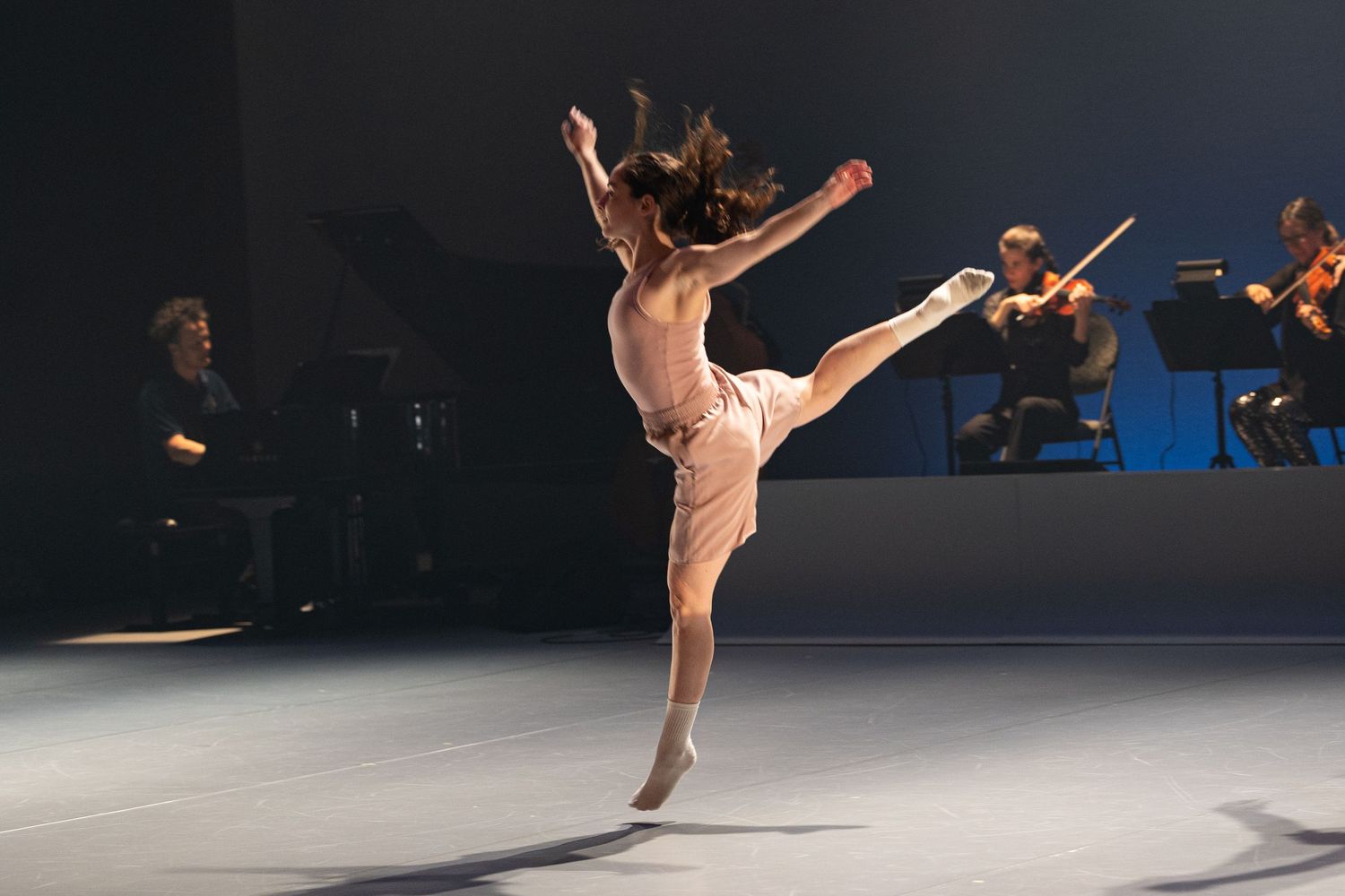 A figure skater performs a graceful pose while ice skating in dramatic lighting during a performance.
