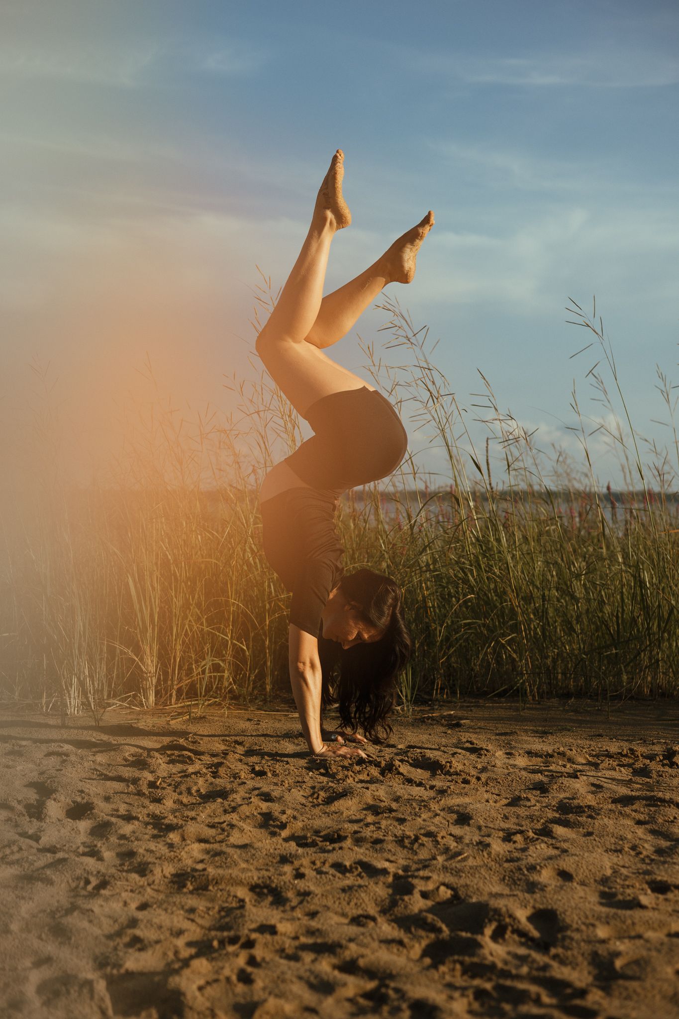 A sequence of silhouettes shows someone performing a cartwheel on a sandy beach at sunset with tall grass in background.