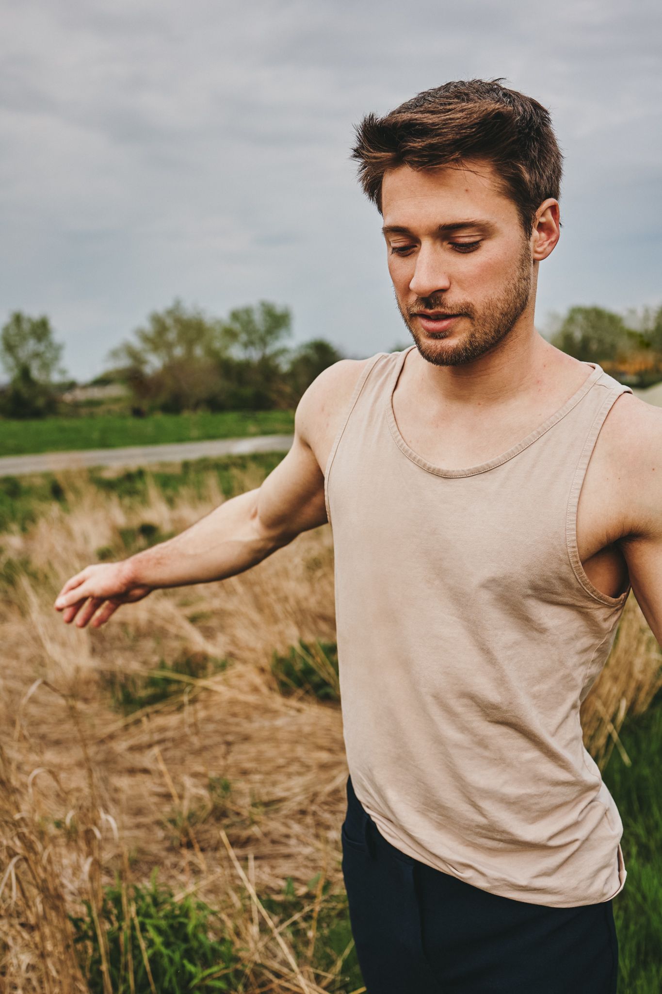 A person in a beige tank top standing in a grassy field with an outstretched arm on an overcast day.