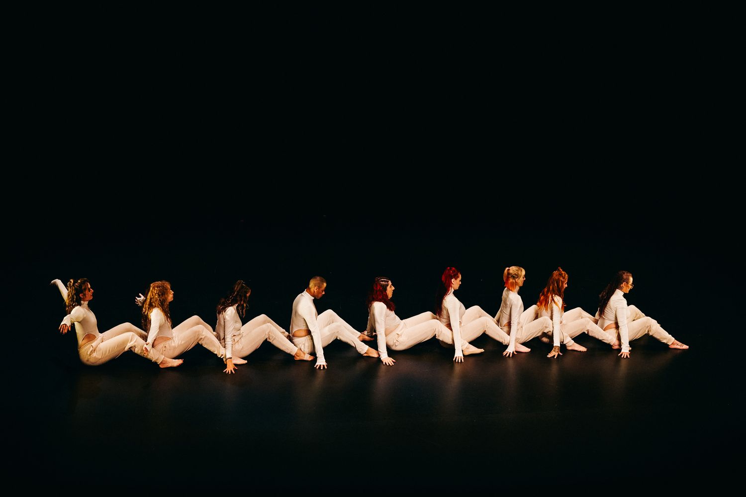 Silhouetted dancers lying on dark stage floor posed in graceful undulating formation with spotlights.