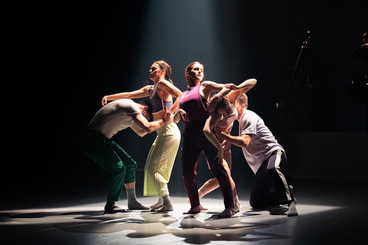 Dancers perform a dynamic contemporary dance piece under dramatic spotlight on a dark stage.