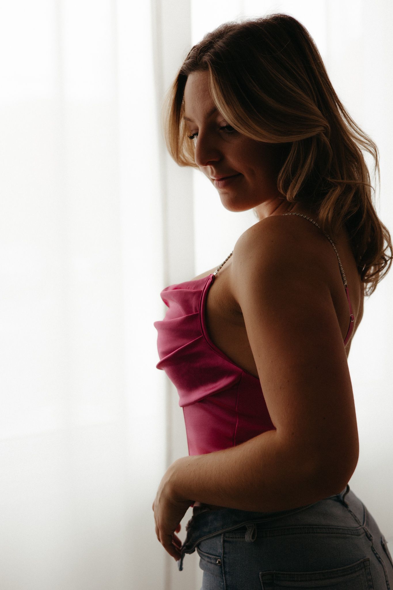 Side profile silhouette against window light of person in pink camisole top and jeans with flowing hair.