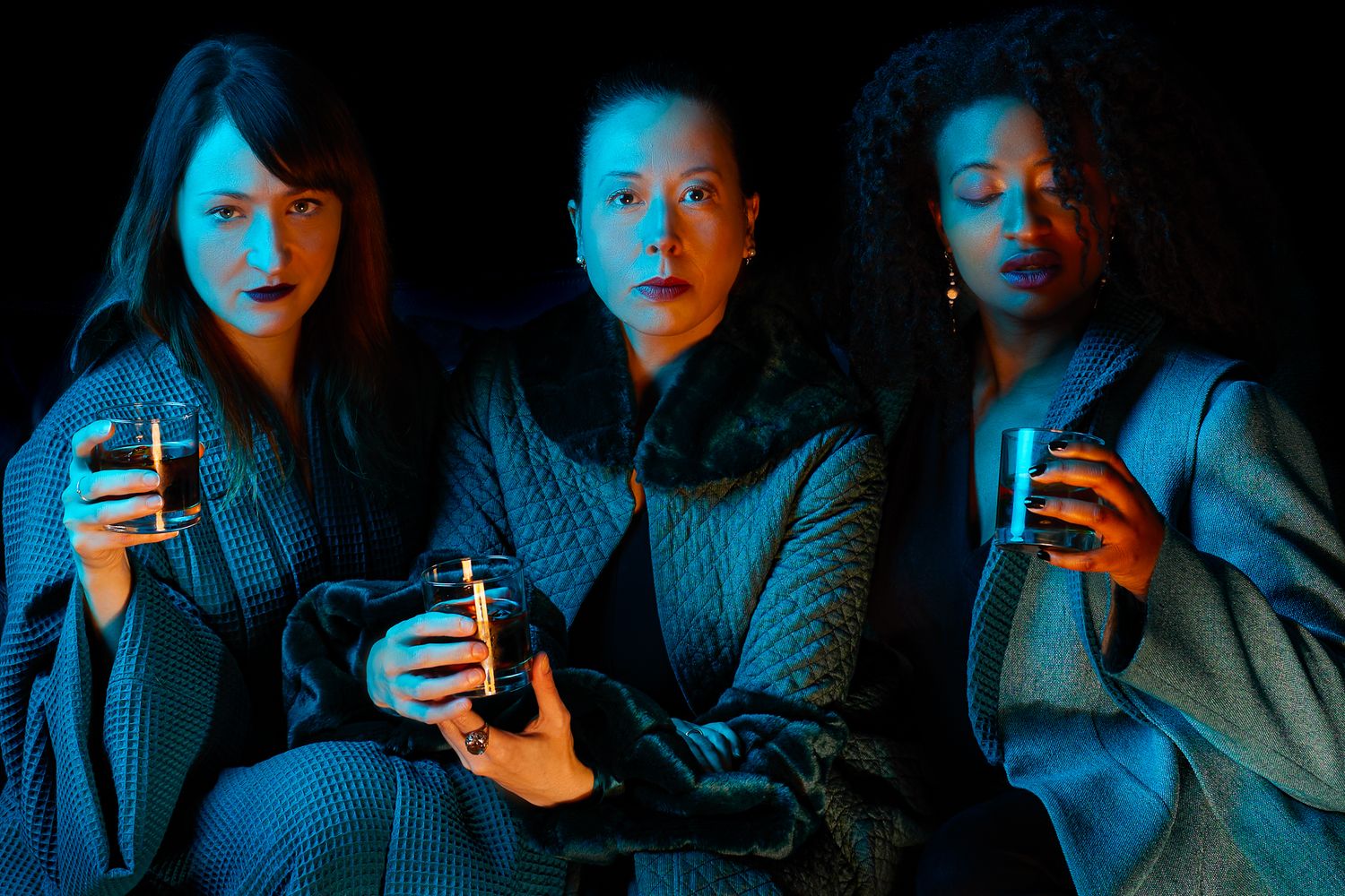 Three friends holding drinks in a dark room bathed in blue lighting creating a moody atmospheric scene.