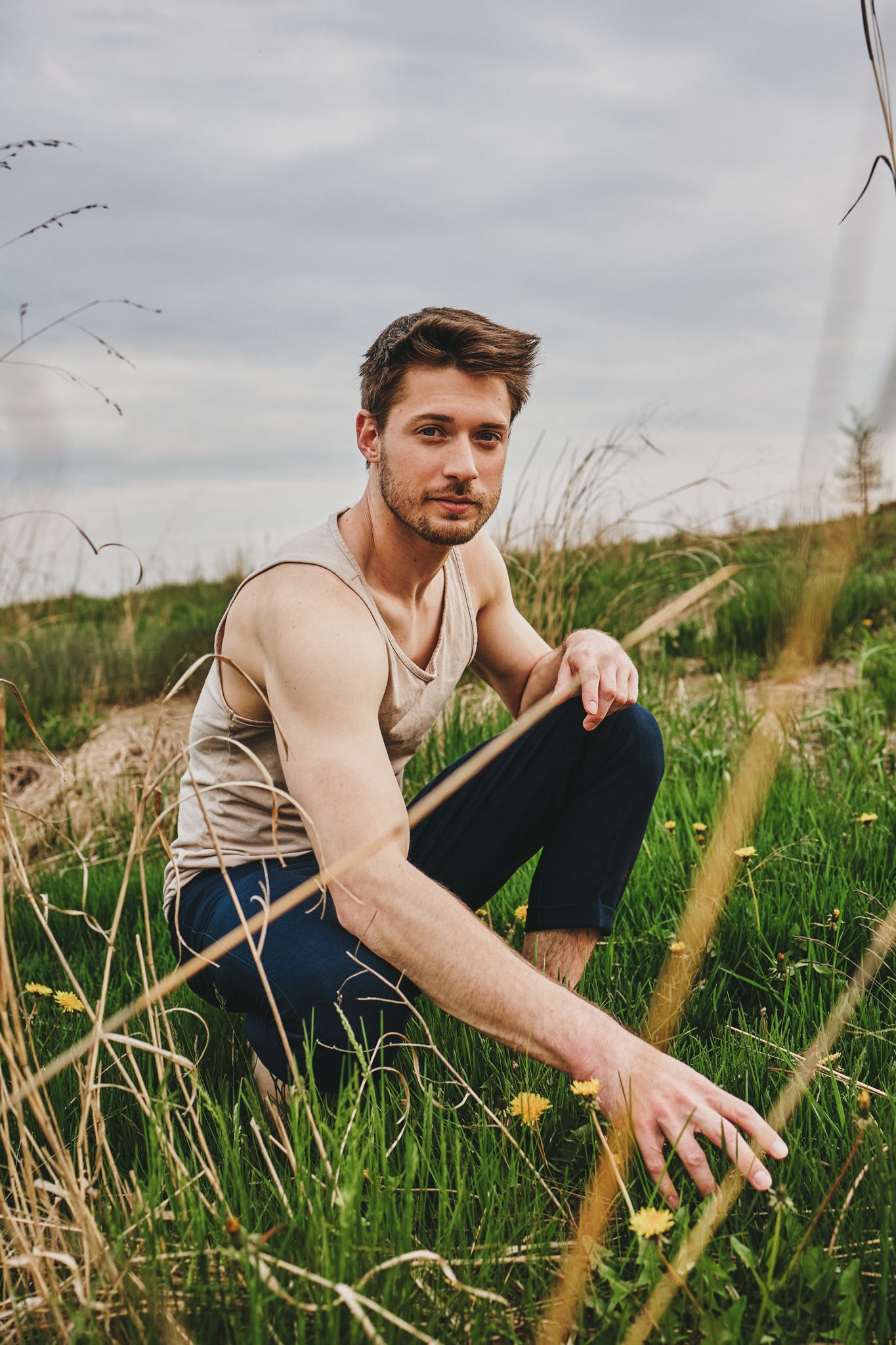 Person relaxing in a grassy meadow with tall grass and wildflowers under cloudy skies.