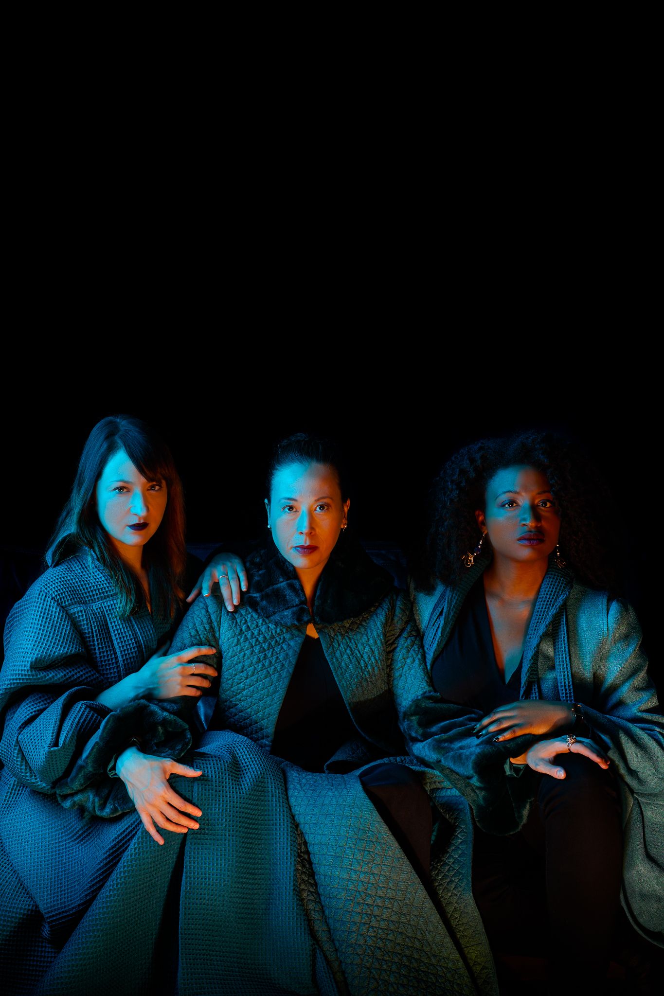 A dark moody sequence of people lit in blue and orange tones watching something intently in a suspense-filled scene.