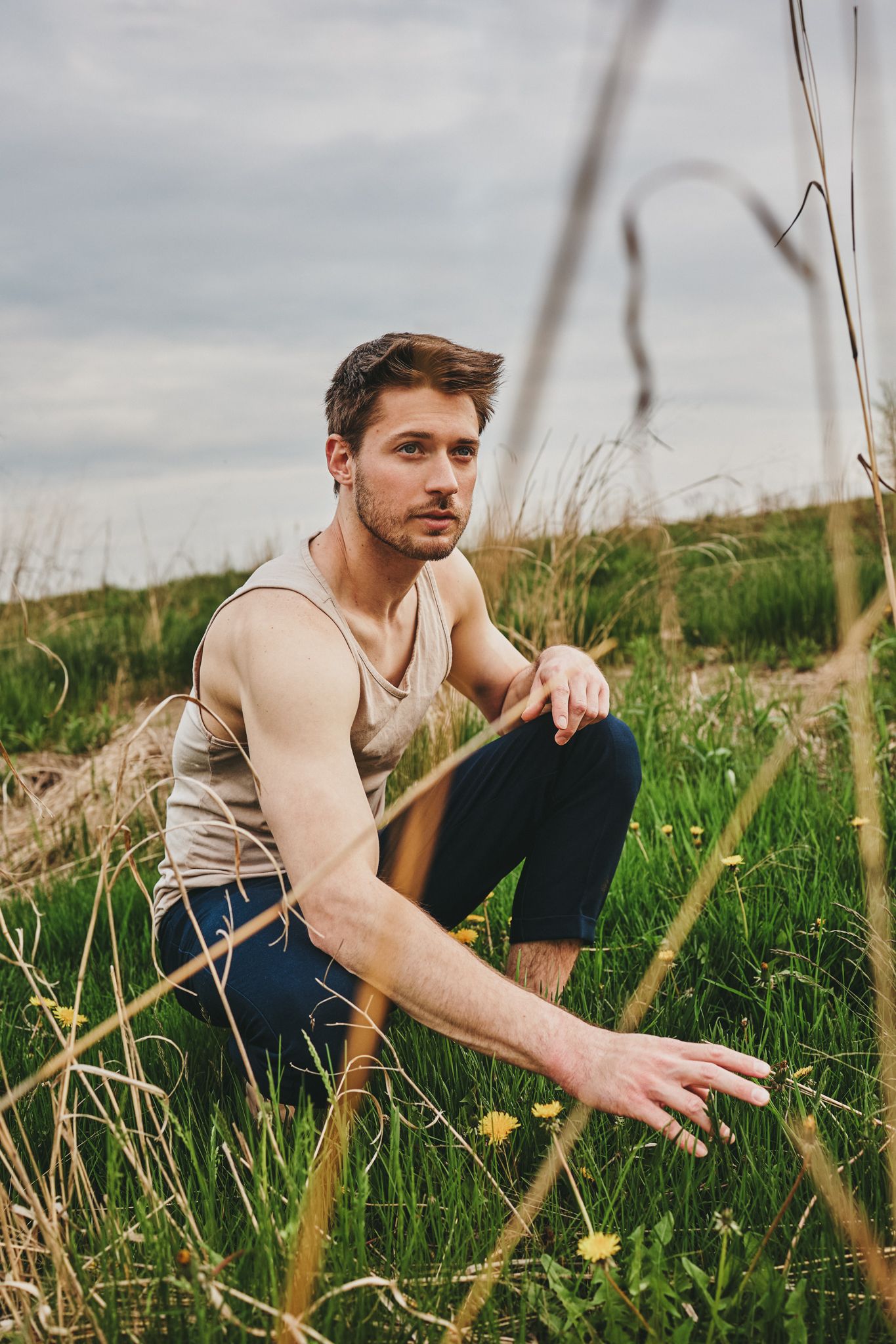 Person sitting in a grassy meadow with wildflowers wearing a beige sweater against a cloudy sky.