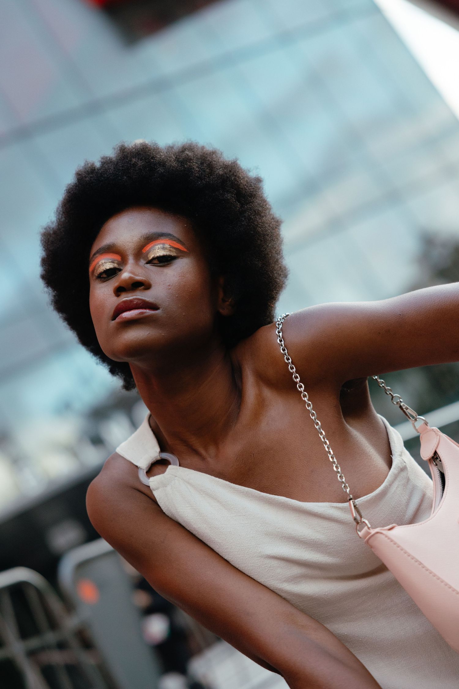 Portrait of someone with natural hair wearing a beige tank top and silver chain necklace against a blurred background.