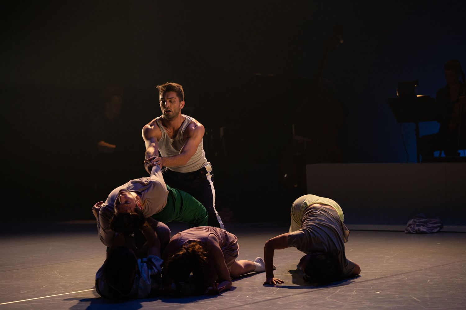Dramatic dance performance on dark stage with low lighting shows dancers in emotional contemporary movements.
