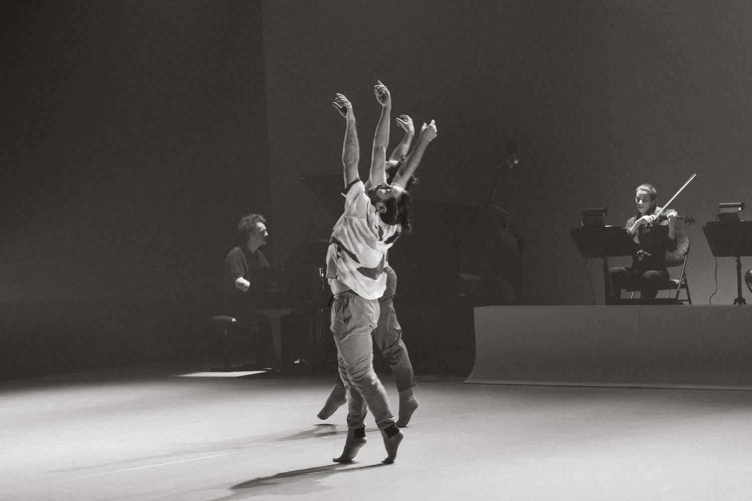 Dancers perform a dynamic series of moves in monochromatic silhouettes against a stark background.