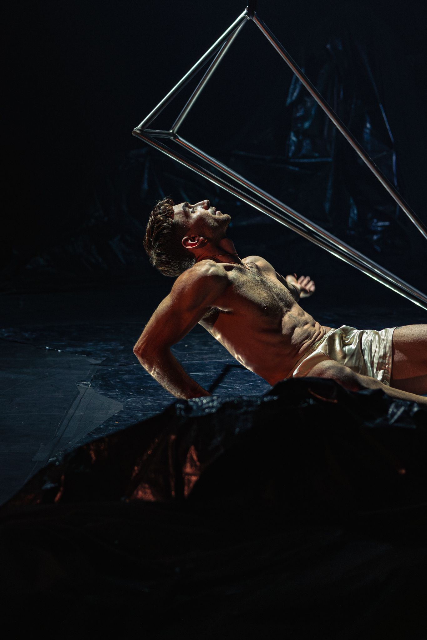 Modern dance performance with dramatic lighting and reflective surfaces showing a dancer in dynamic motion.