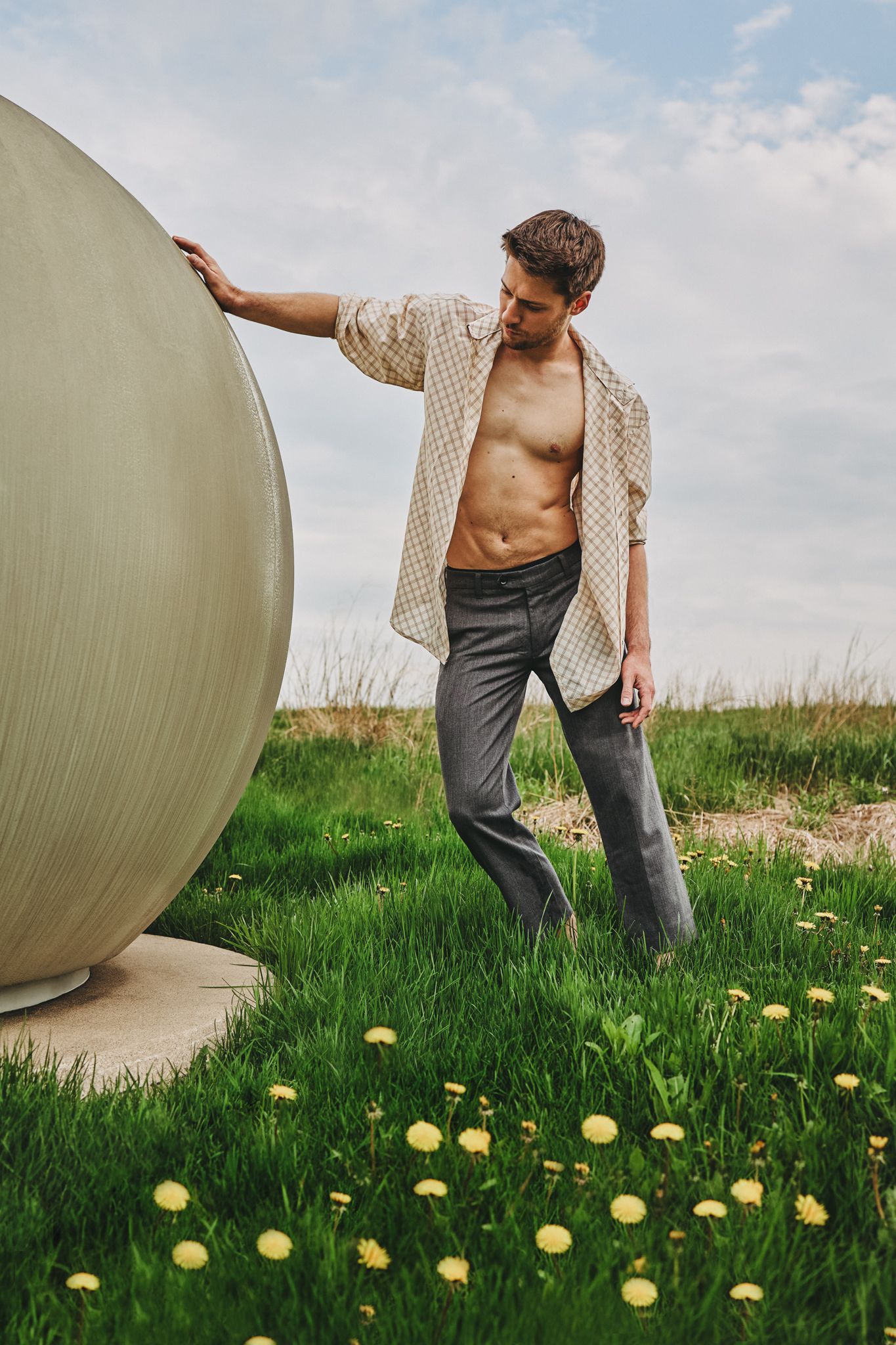 Person in cream cardigan performing artistic movement with large exercise ball in grassy field with yellow flowers.