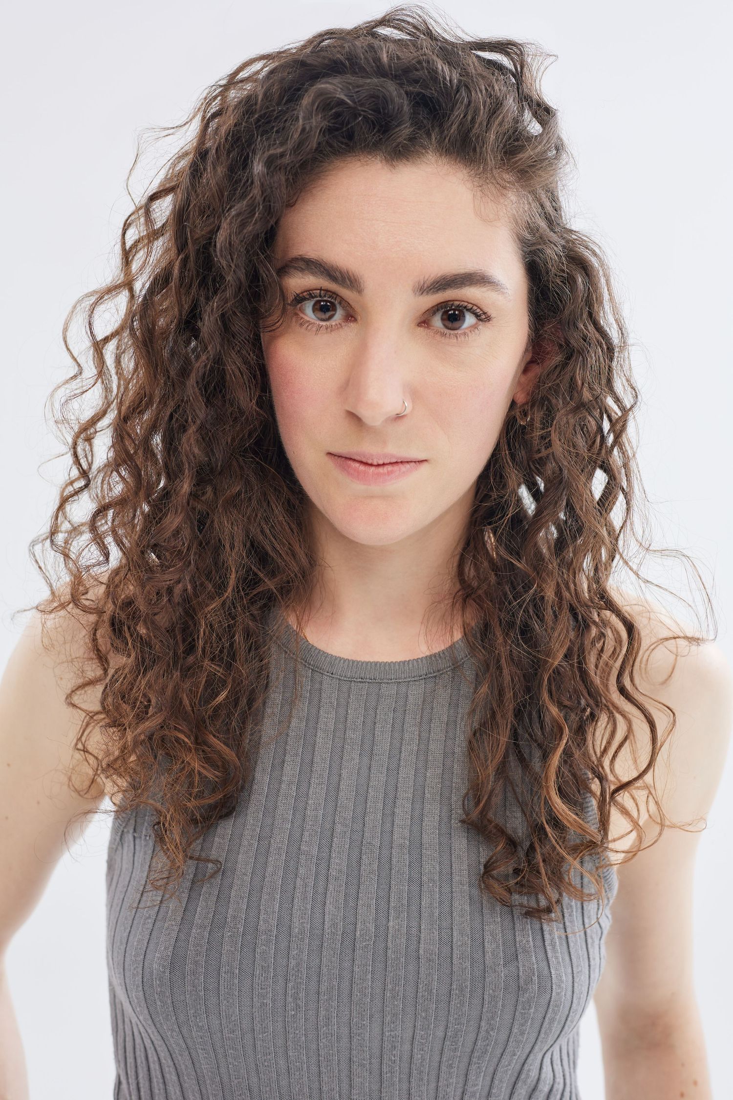 Portrait of curly-haired person in gray ribbed tank top against white background.