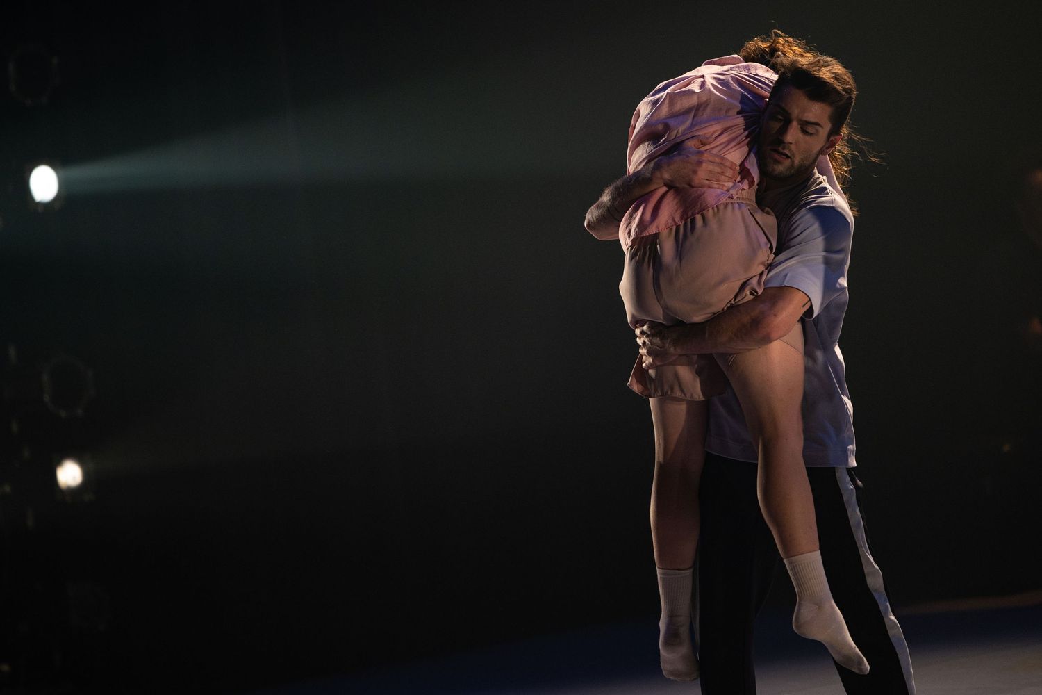 Seven figure skaters perform a dramatic lift sequence on ice in a dimly lit arena setting.