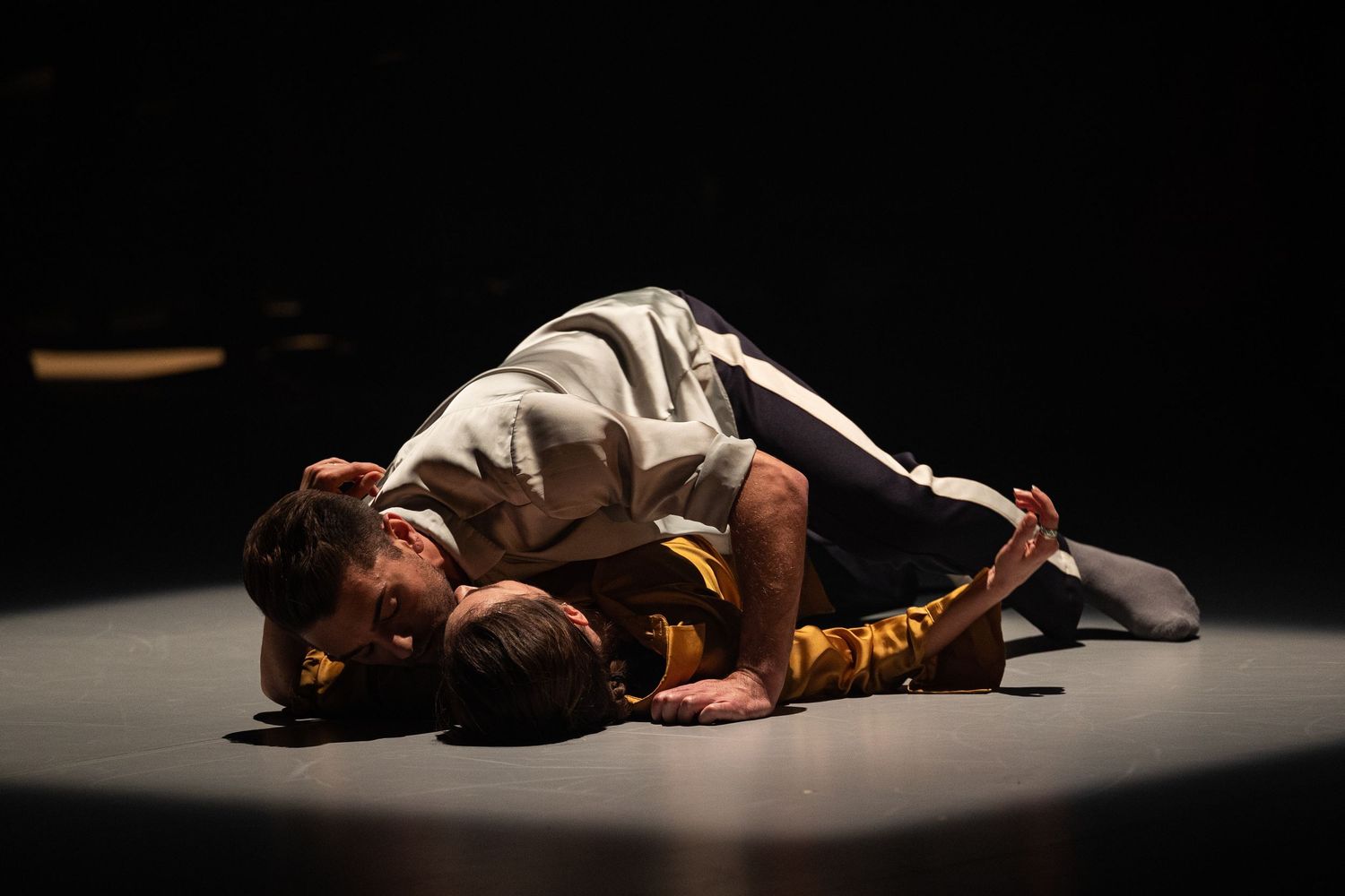 A performer lies motionless on stage in dramatic lighting during a contemporary dance performance.