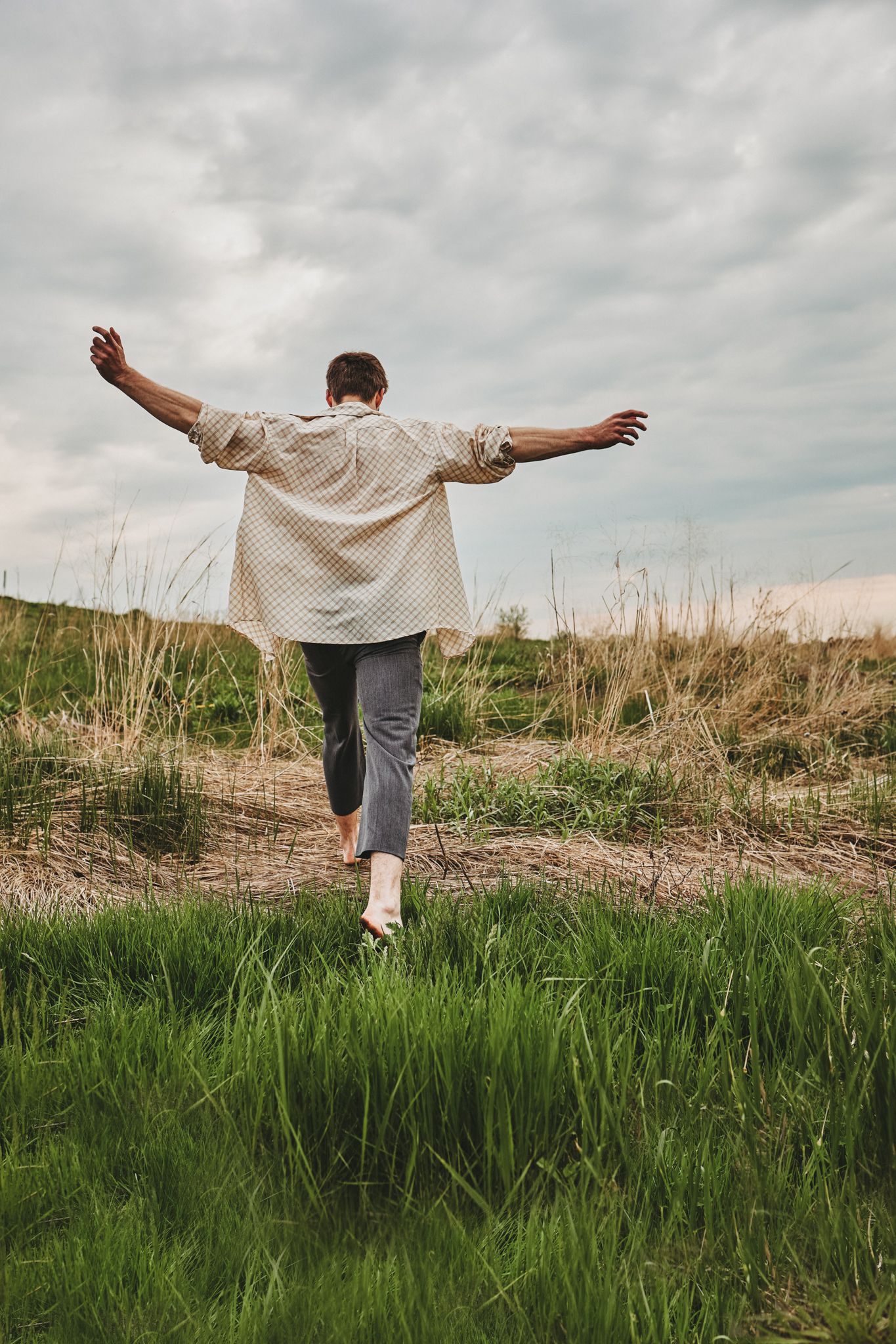 A person stretches their arms out wide while standing in tall grass on a cloudy day in nature.