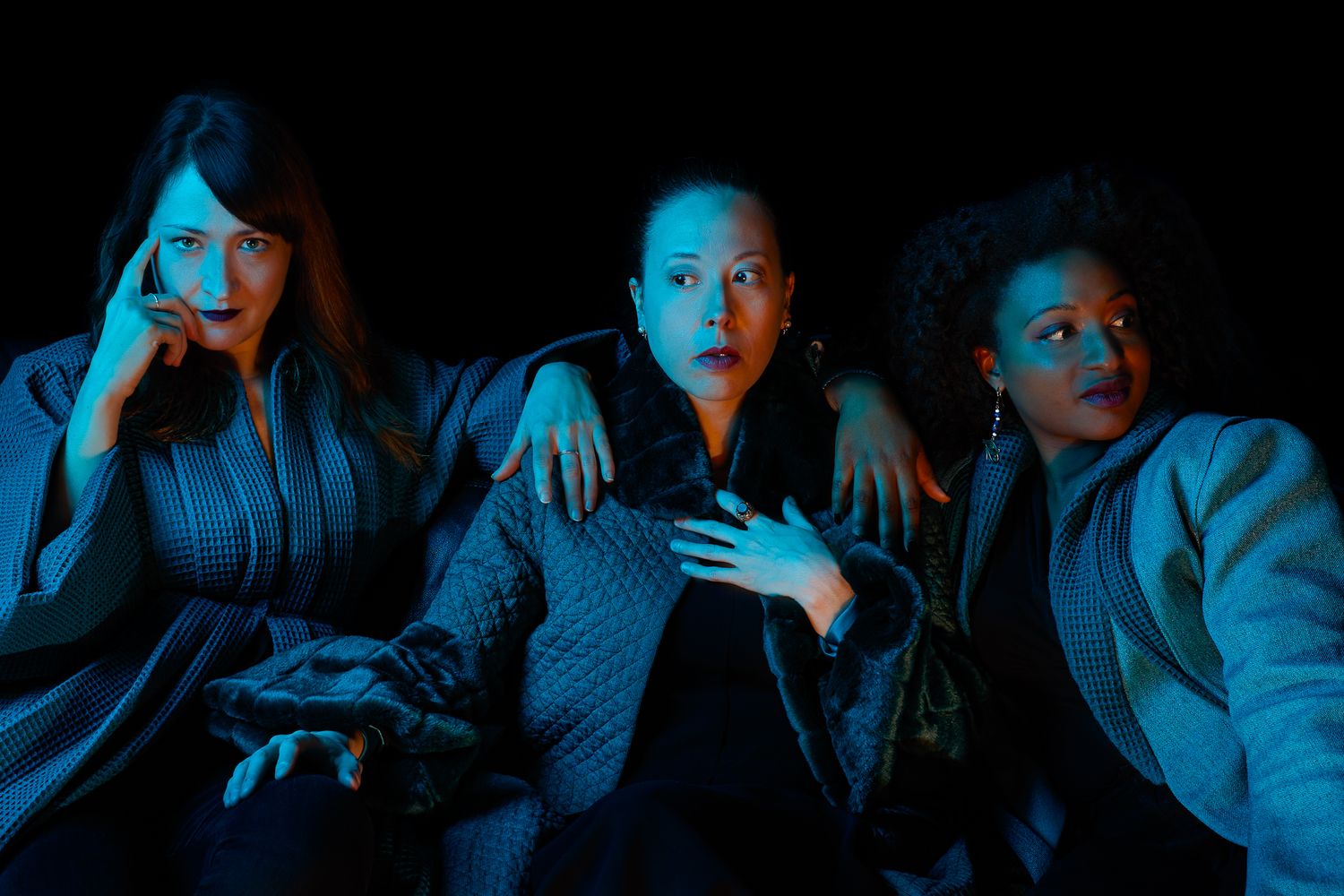 Three people sit together under dramatic blue lighting creating a moody atmospheric scene.