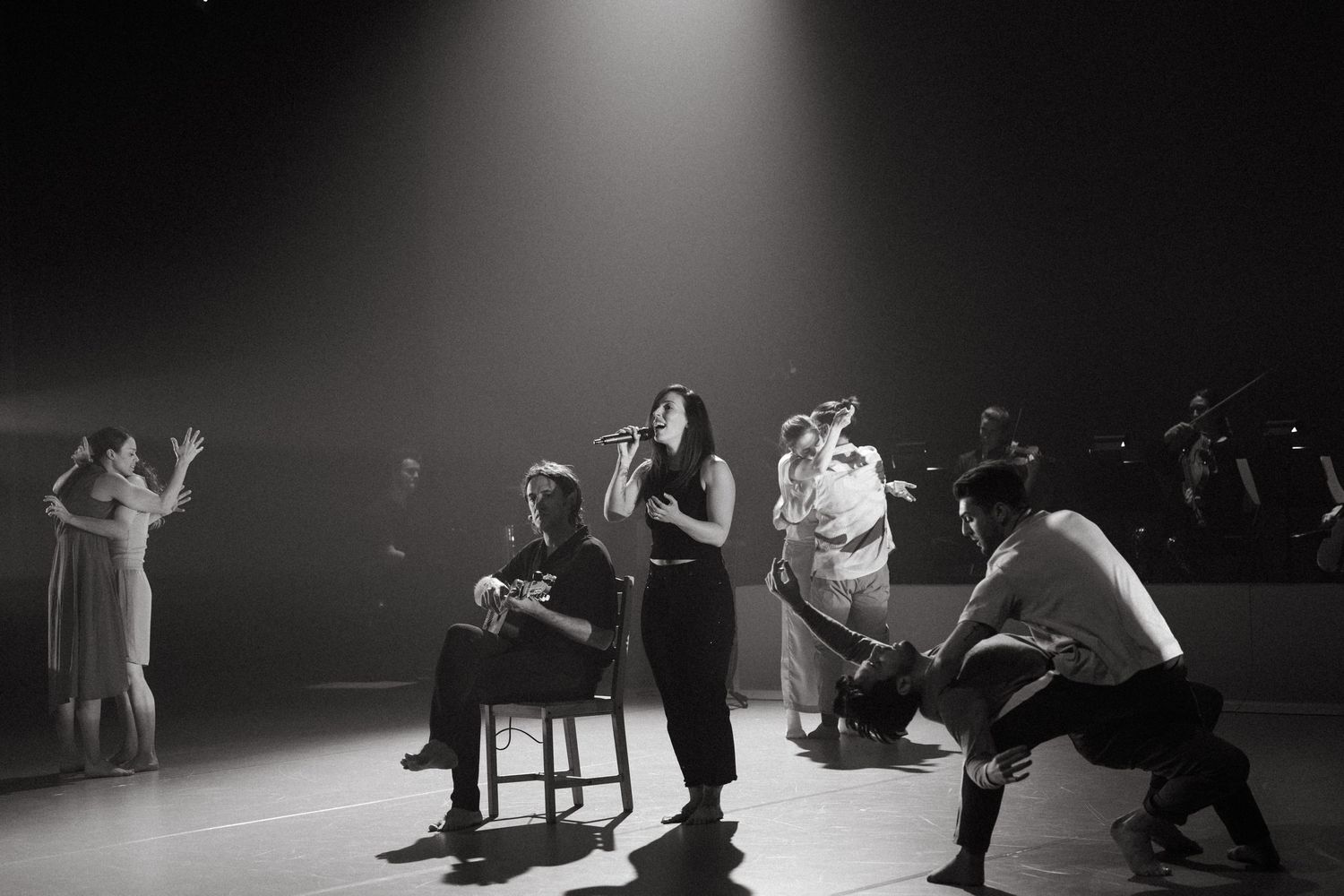 Dancers perform an emotional contemporary dance piece on a dimly lit stage with dramatic lighting.