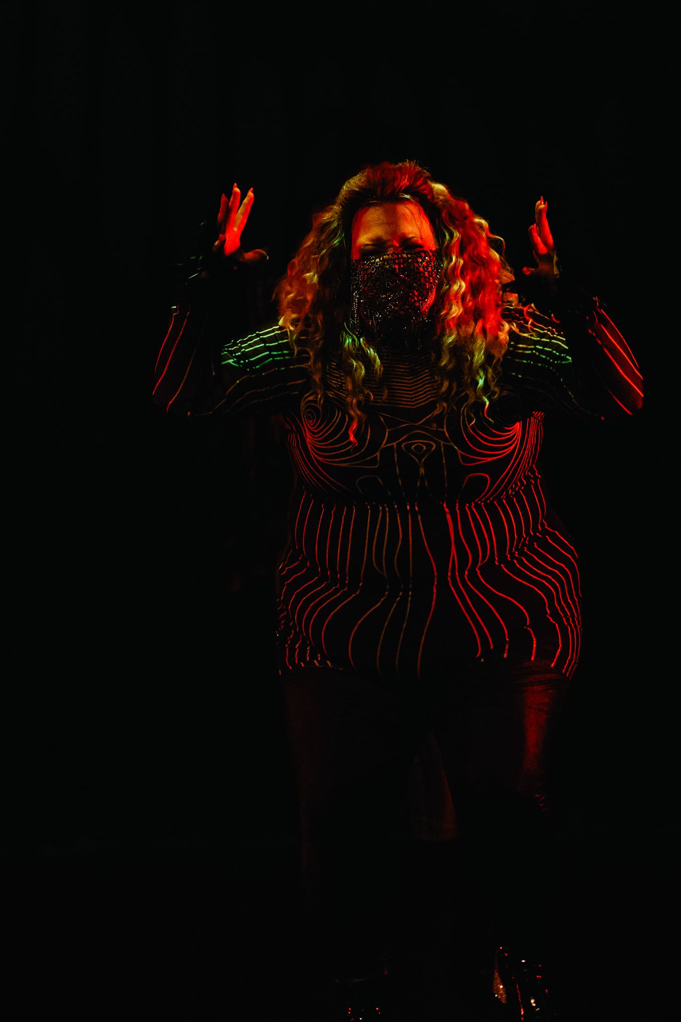 Artistic dark portrait with red neon lighting illuminating a figure against black background in dramatic pose.