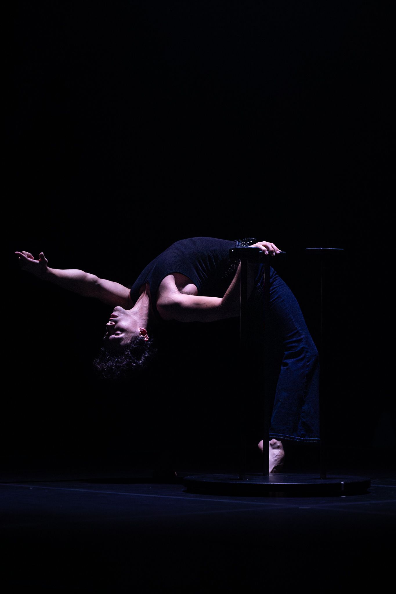 A contemporary dancer performs a backward arching movement sequence in a dark theater setting.