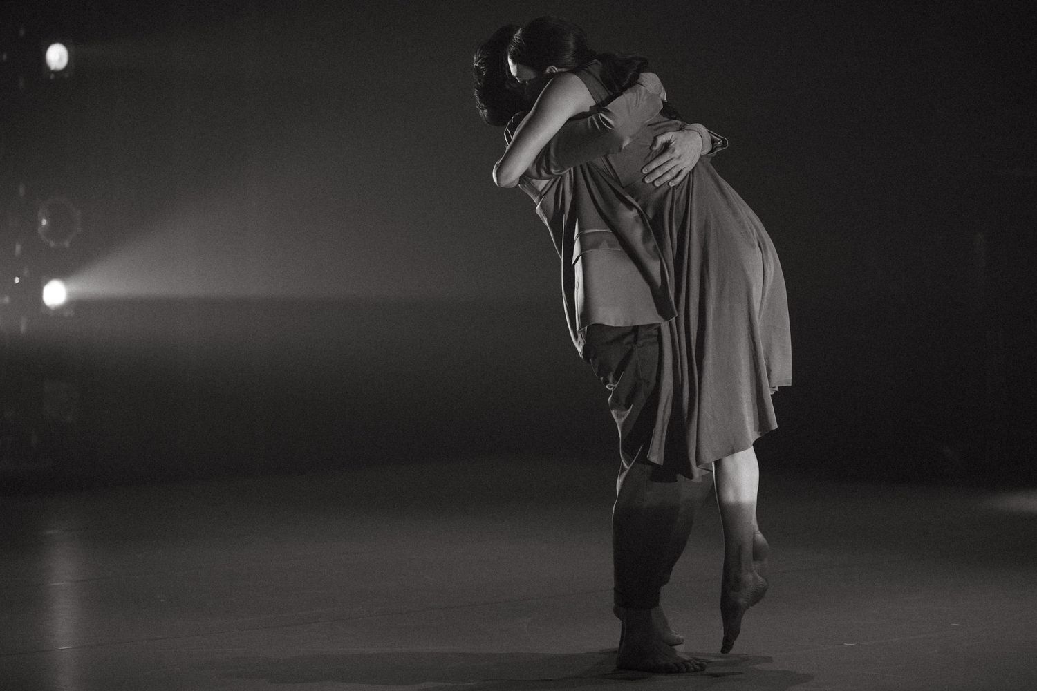 Black and white sequence shows dancer in flowing robes performing graceful movement in dim spotlight on stage.