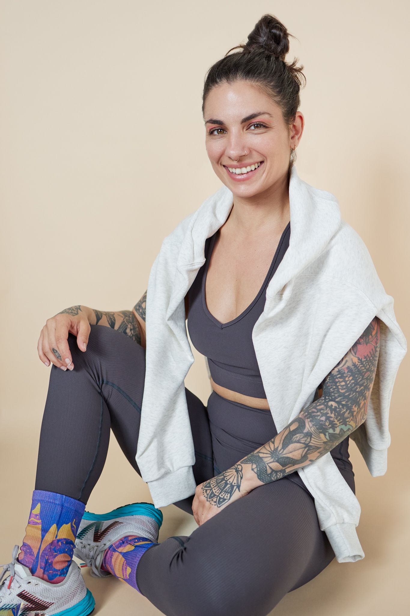 Athletic model in workout attire shows off colorful socks and tattoo sleeve while wearing grey leggings and white jacket.