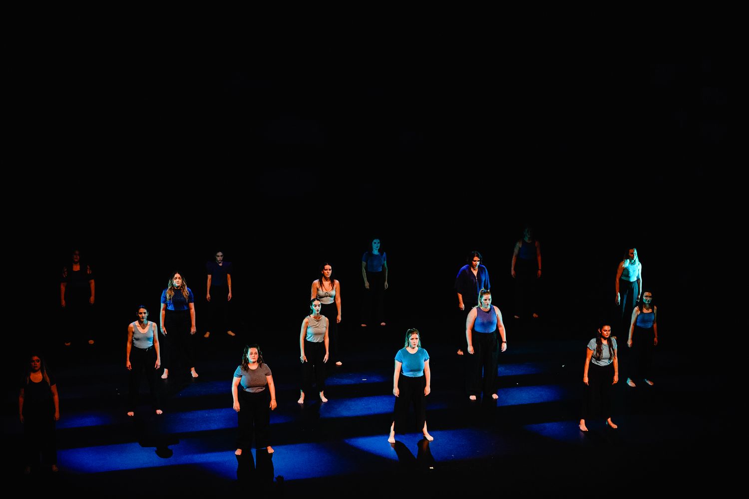Dancers stand in dramatic spotlights on dark stage during contemporary dance performance.