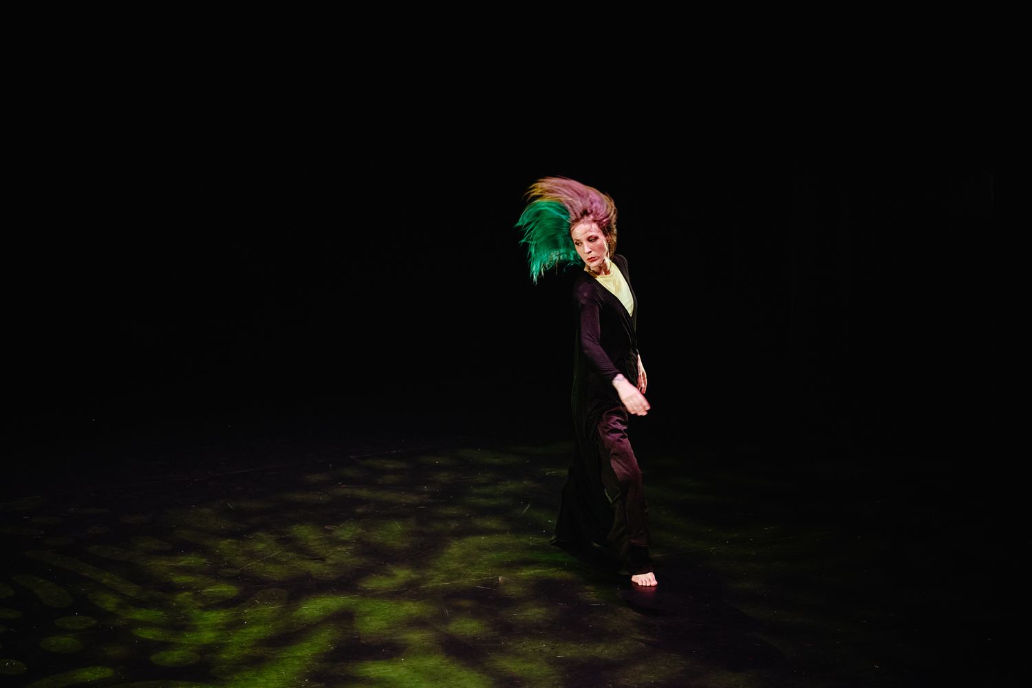 A figure dances gracefully through darkness against a black background with subtle green illumination.