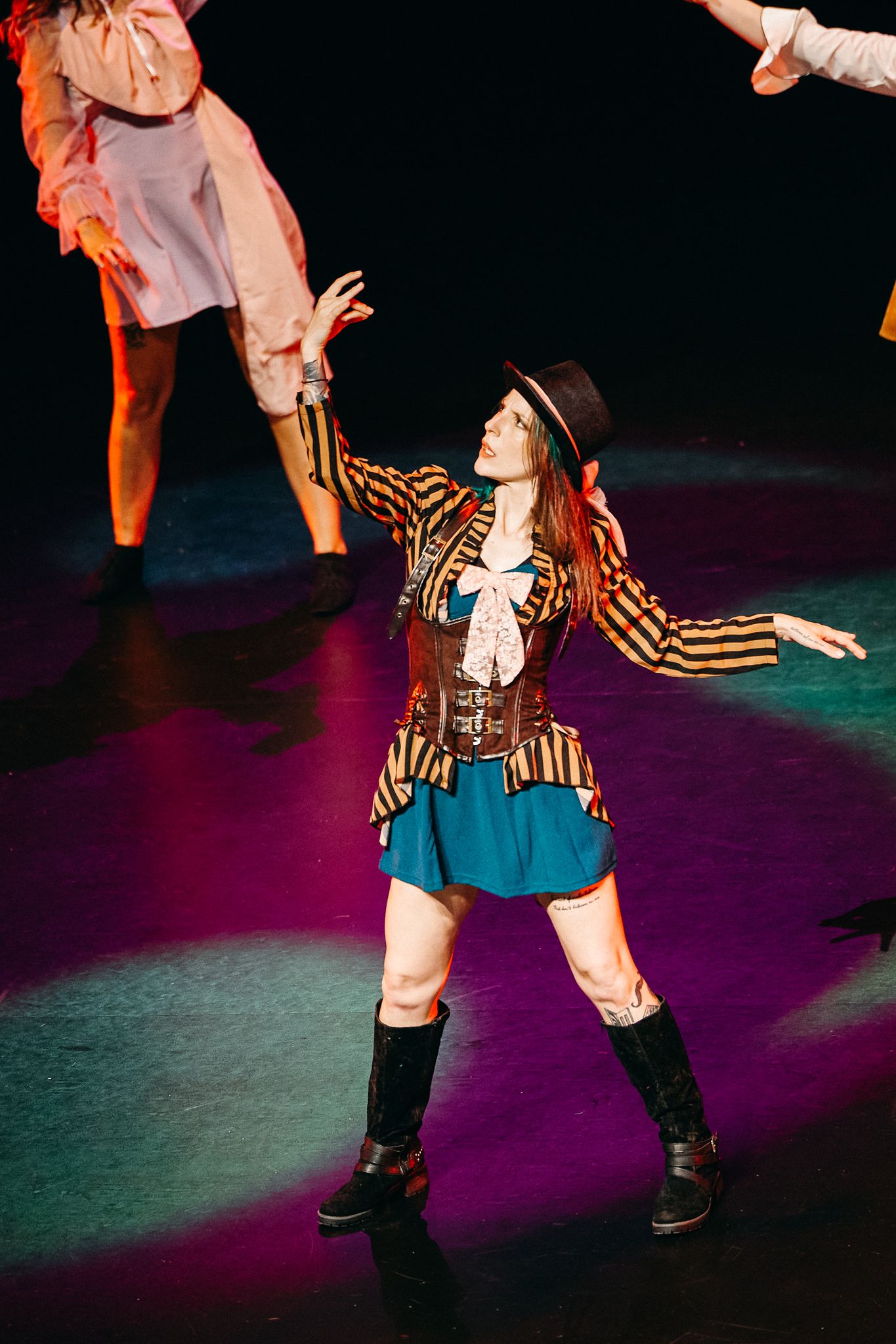 A performer in a striped jacket and boots strikes dramatic poses during a colorful theatrical production.