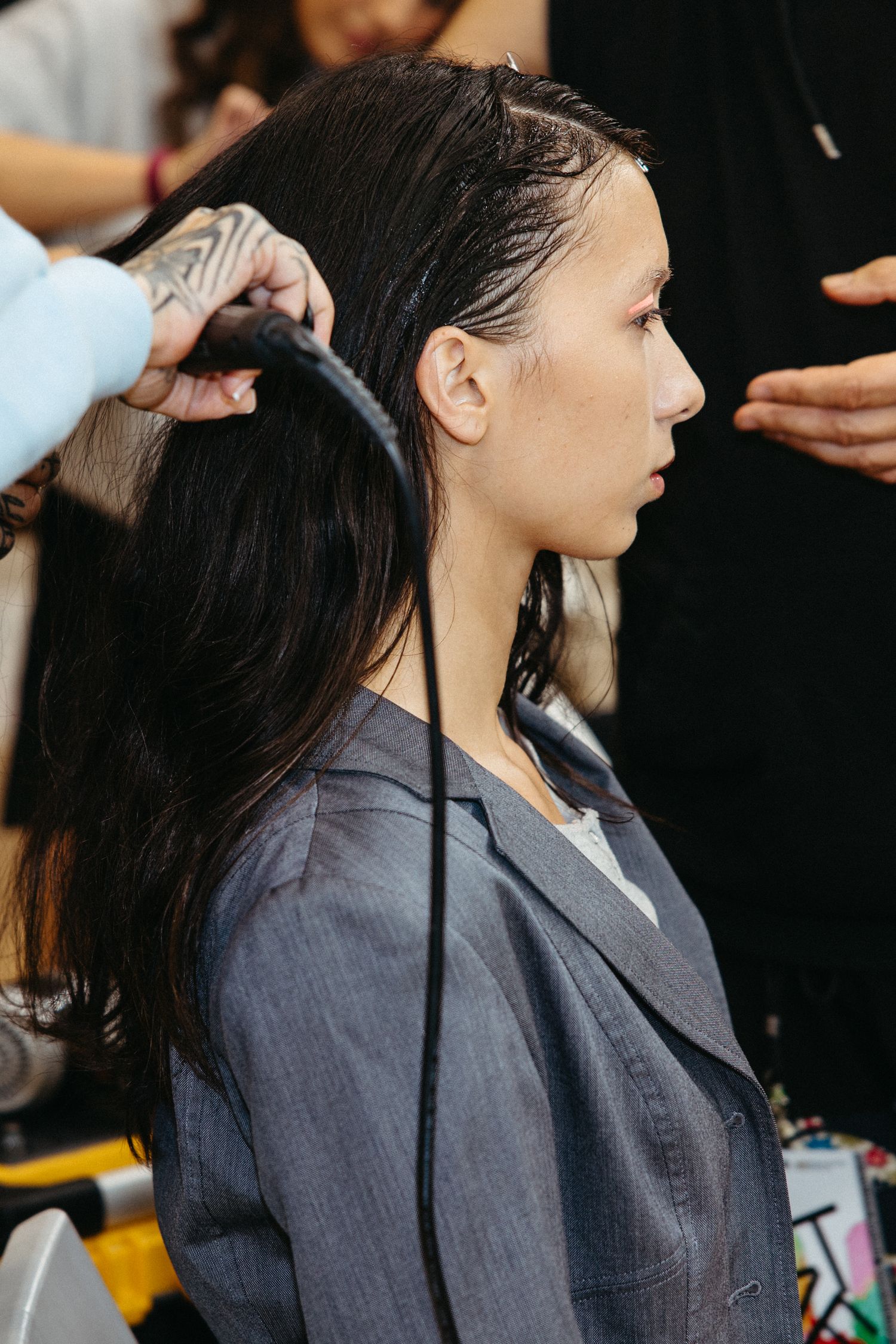 Long dark hair being styled with professional tools backstage at a fashion show.