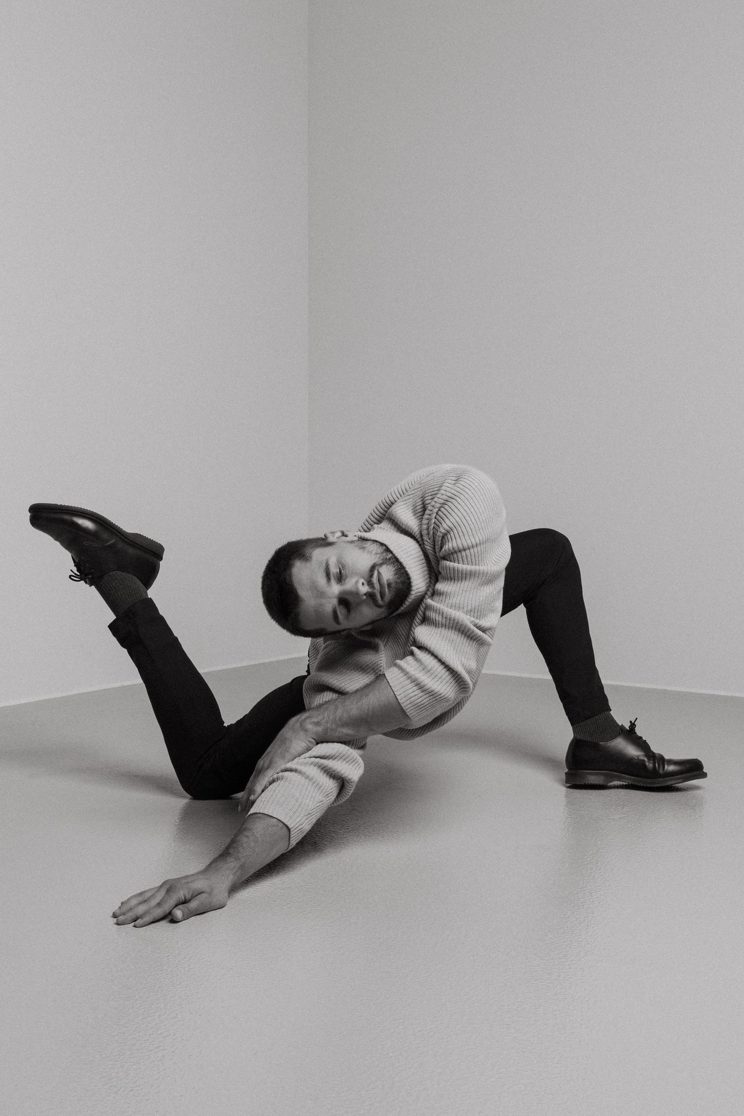 Series of grayscale photos showing someone lying on ground against wall in various artistic poses wearing cream sweater and dark pants.