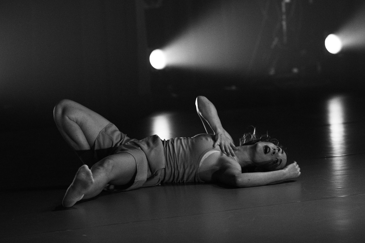 A ballerina lies gracefully on a dark stage floor in soft theatrical lighting during a dramatic performance.