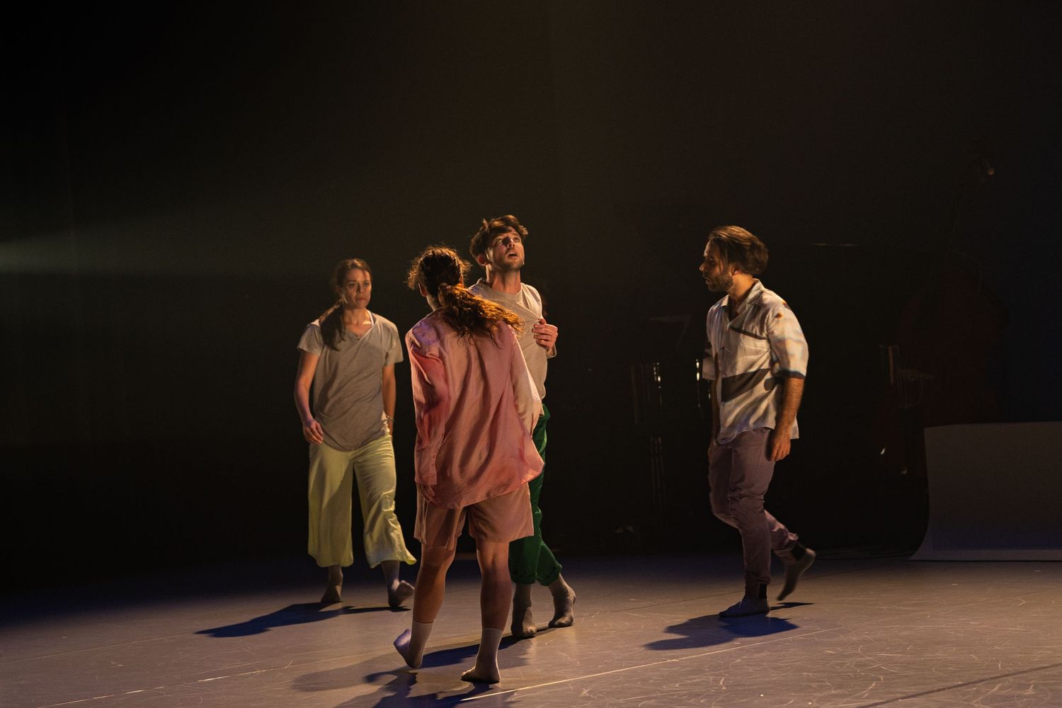 A sequence of choreographed dance movements performed by dancers on a dimly lit stage during a theatrical performance.